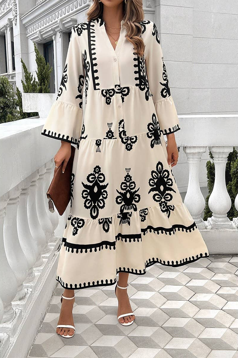 Woman wearing a long, cream-colored dress with black patterns in an outdoor setting.