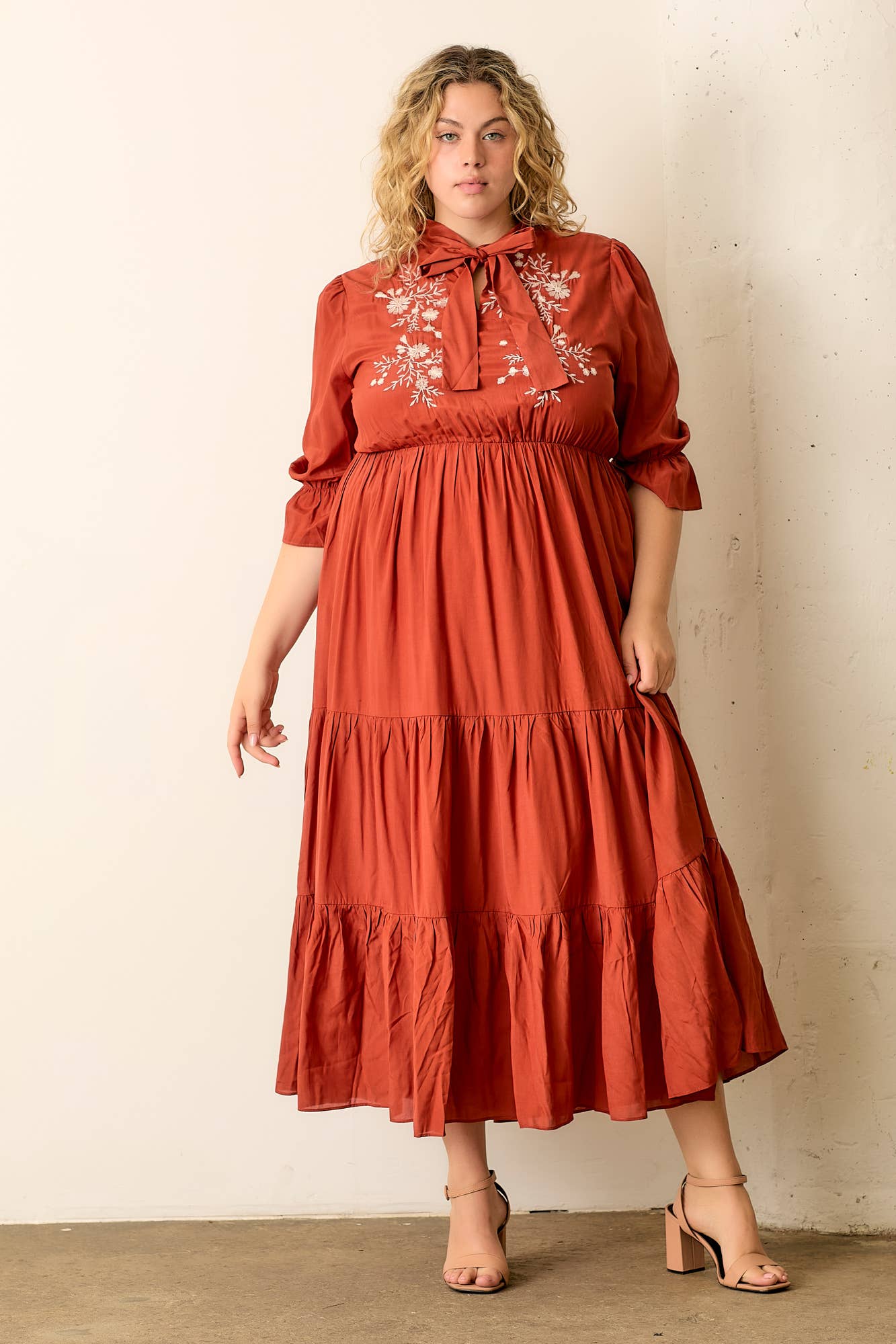 Woman wearing a rust-colored dress with floral embroidery against a plain background