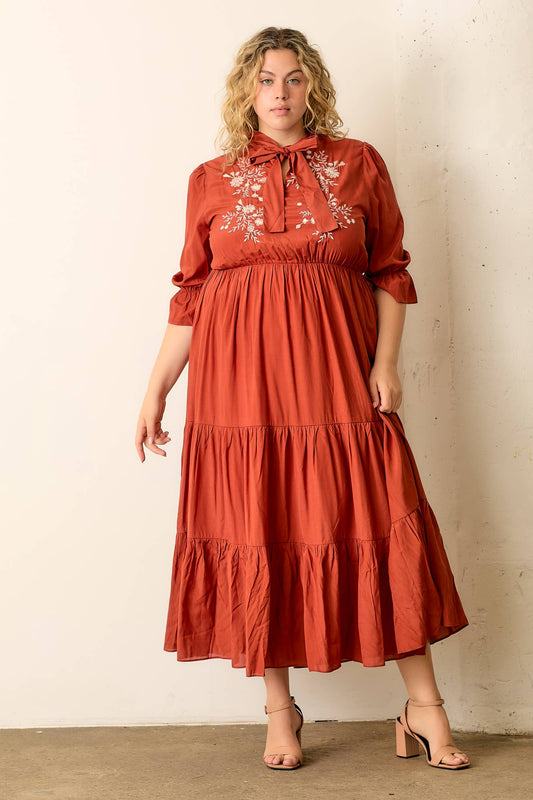 Woman wearing a rust-colored dress with floral embroidery against a plain background