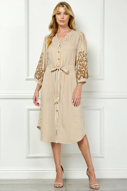 Woman wearing a beige and white striped dress with lace sleeves against a white wall.