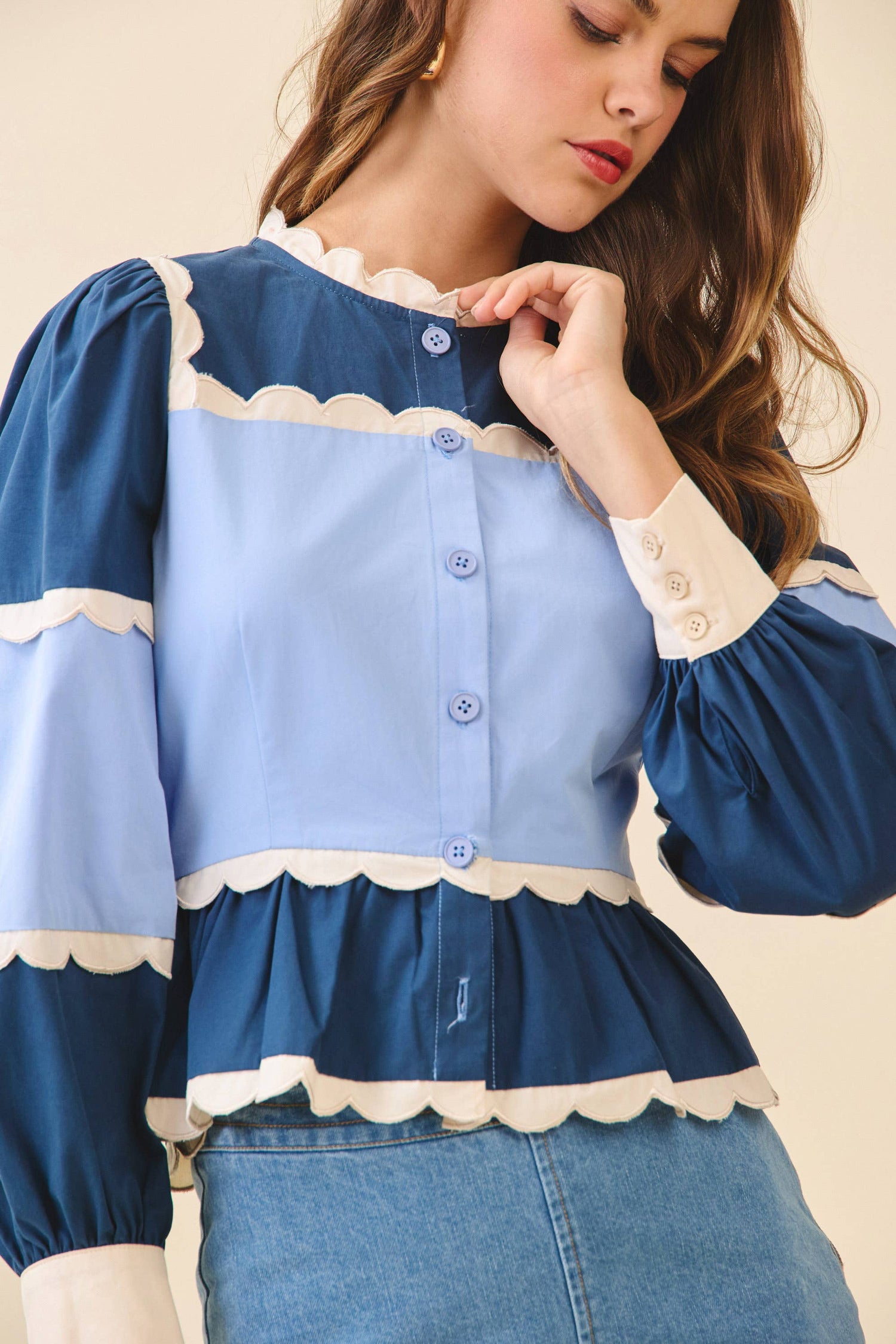 Woman wearing a blue and white blouse with ruffled details on a beige background